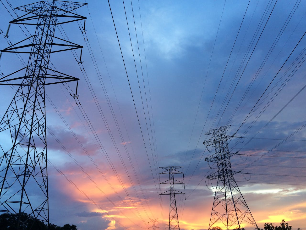 services-04 A scenic view of high voltage power lines silhouetted against a vibrant sunset sky.